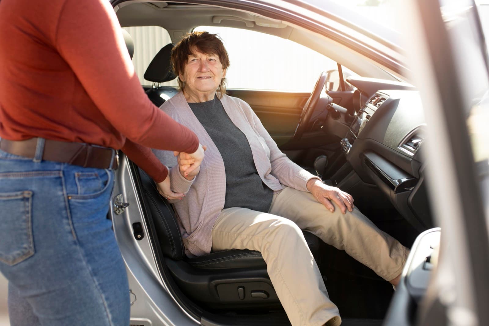 The driver steadies a rider's hand as she settles into the seat, the door held open in morning light.