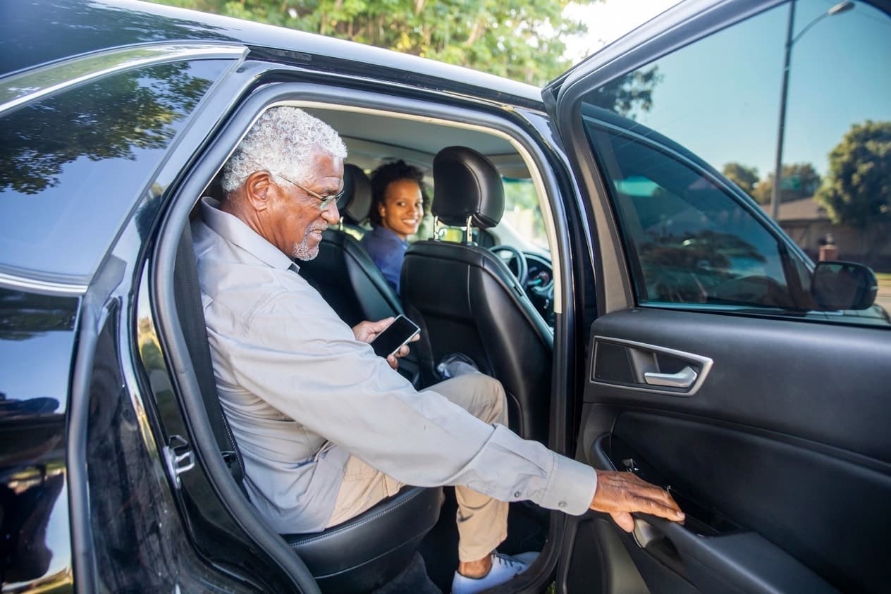 A rider settles into the back seat and reaches for the door; the driver is already turned round at the wheel, waiting.